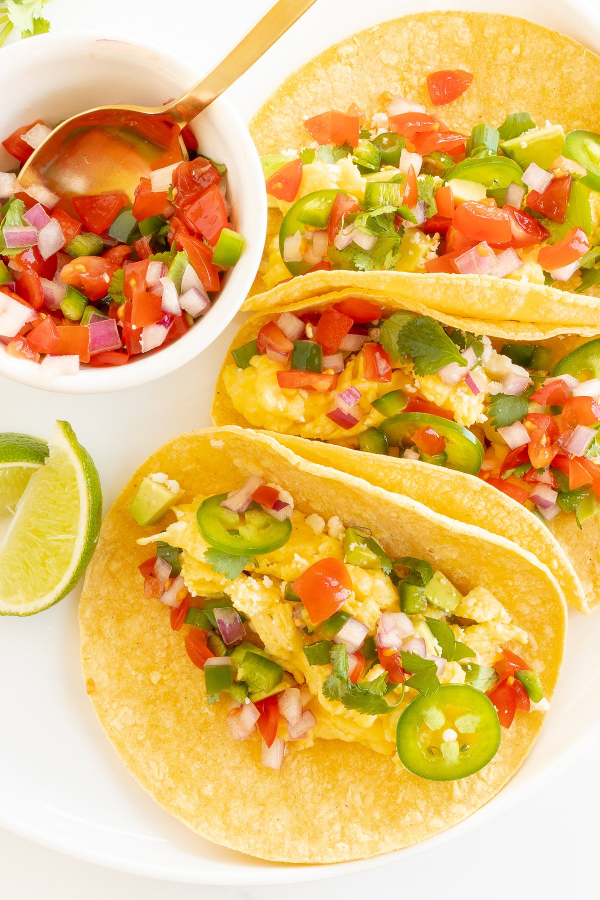 Egg breakfast tacos in corn tortillas with a bowl of salsa to the side.