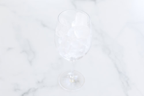 A wine glass filled with ice cubes is placed on a white marble surface.