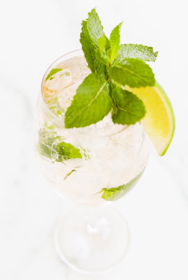 A glass of iced rosé spritz with lime slices and fresh mint leaves on a white background.