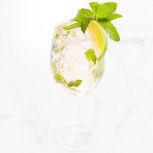 A glass filled with a Hugo Rosé Spritz, ice cubes, mint leaves, and a lime wedge garnish.