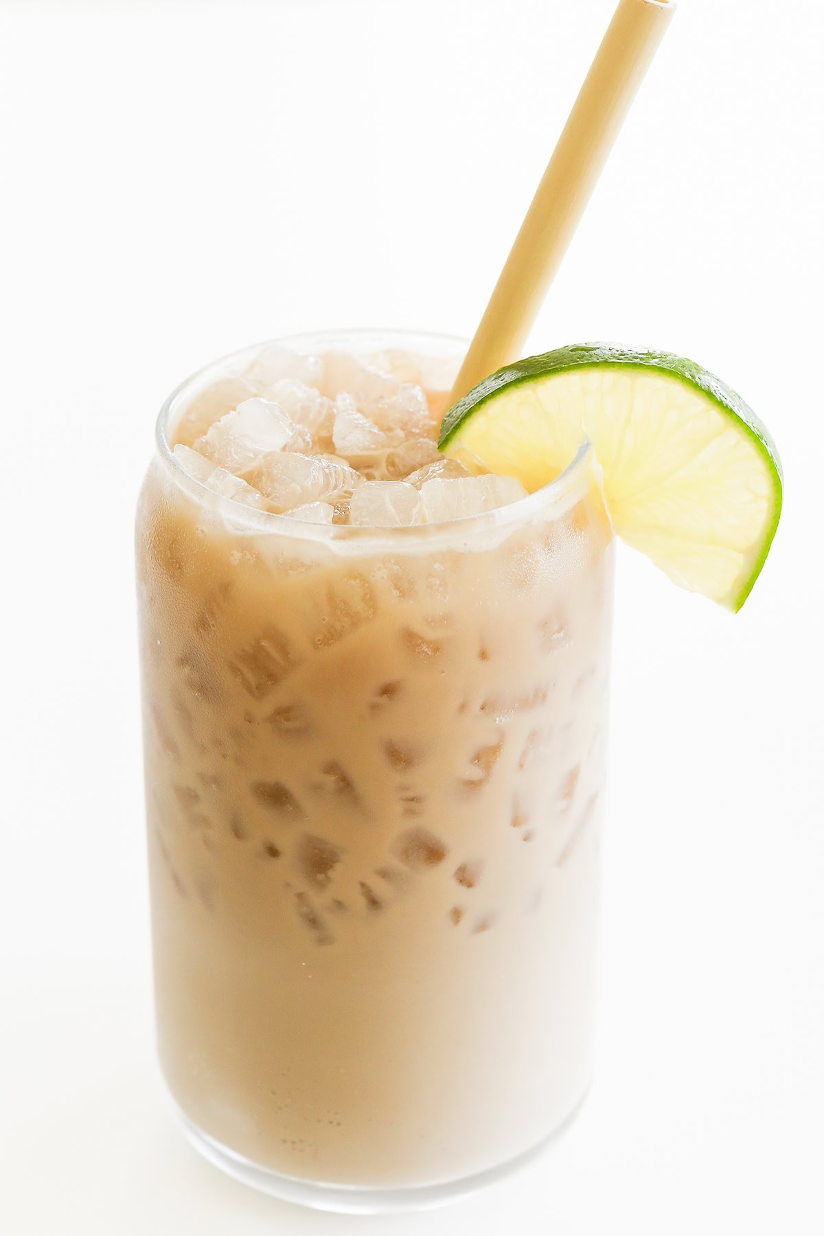 A tall glass of iced Dirty Dr Pepper with a bamboo straw is garnished with a lime slice.