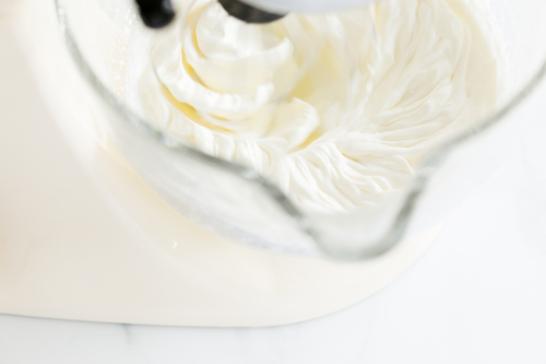 Close-up of a stand mixer bowl with white cream being whipped, creating swirling patterns reminiscent of gooey butter cake ice cream.