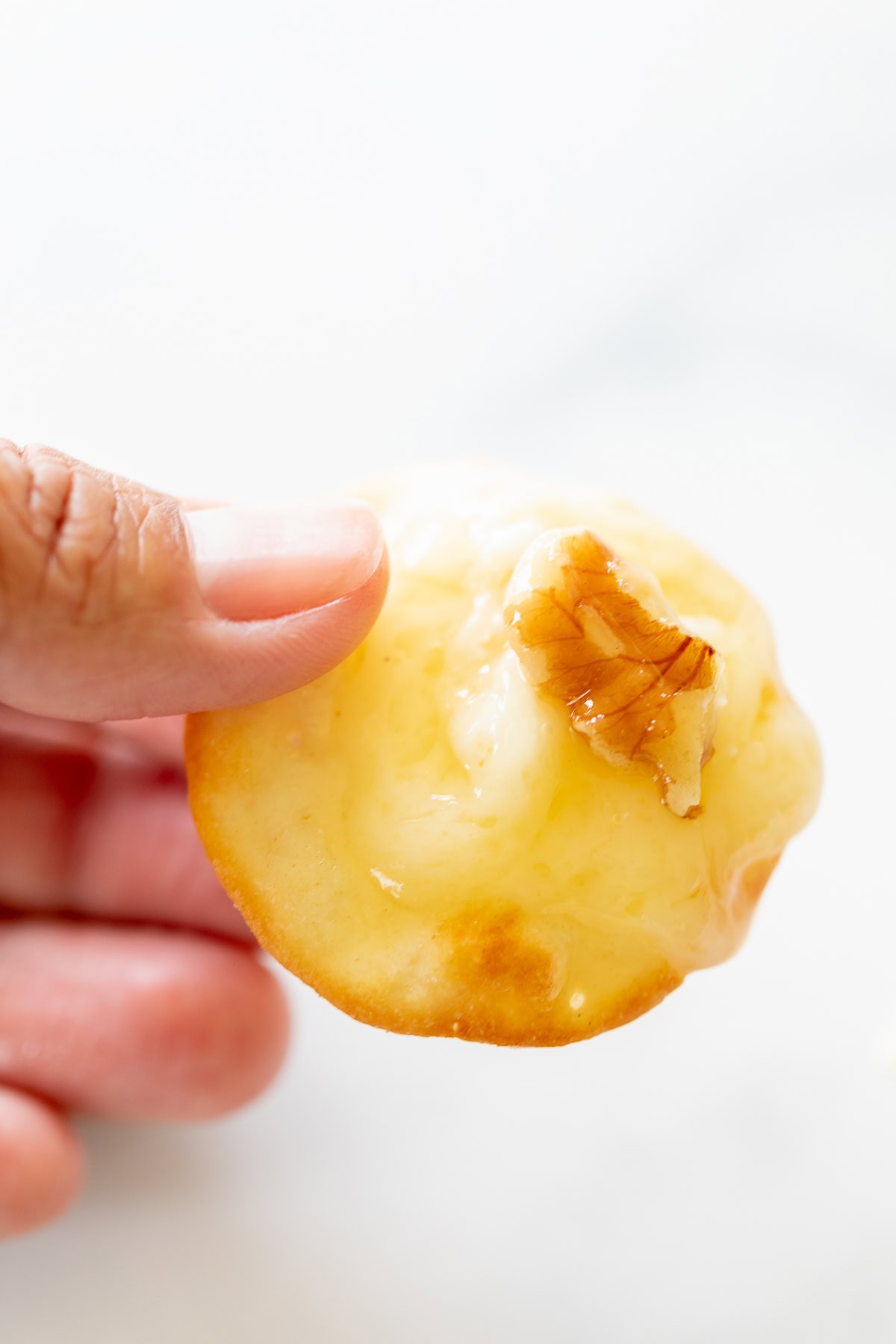 A hand holding a cracker topped with melted cheese and a small piece of nut.