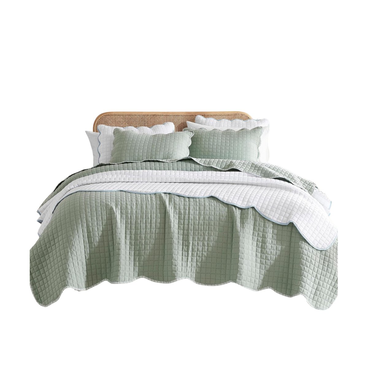 A neatly made bed with a wicker headboard showcases a green and white quilt paired with matching pillows edged in wavy design, offering a Pottery Barn look for less.