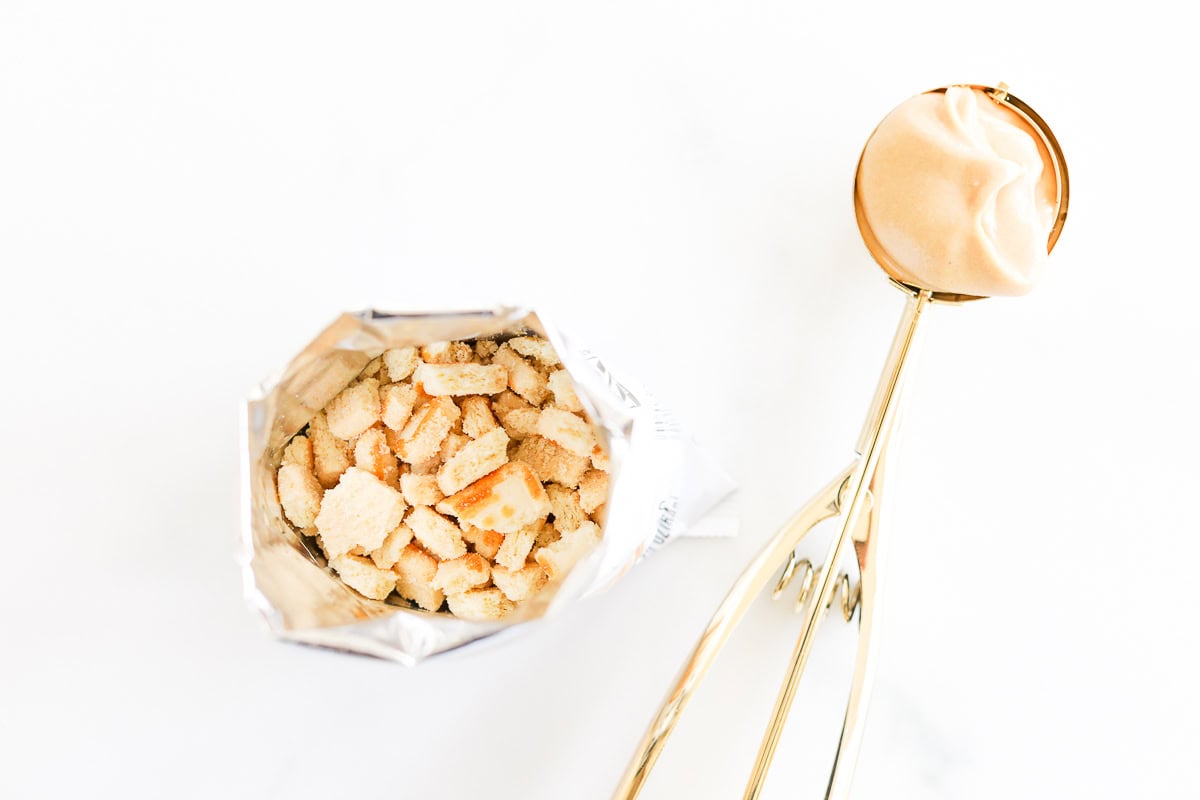 Open bag of crushed cookies next to a gold ice cream scoop with a scoop of peanut butter pie filling