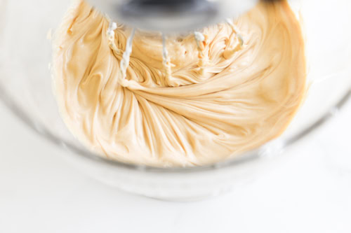 Close-up of creamy peanut butter being mixed in a glass bowl with a stand mixer.