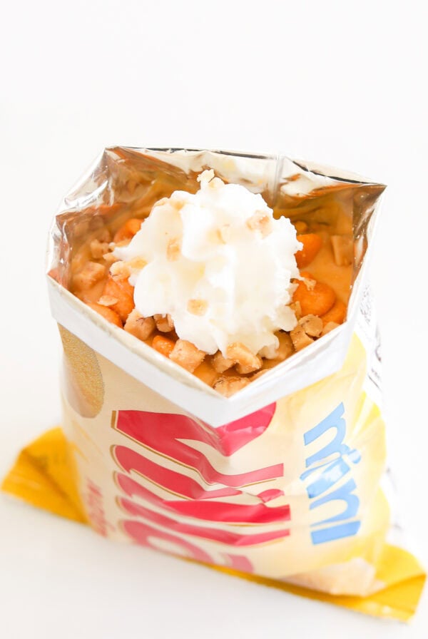 An open bag of chips topped with whipped cream and sprinkled with small toppings, creating a playful twist reminiscent of butterscotch pie in a bag.