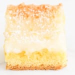 Close-up of a slice of lemon gooey butter cake with a golden crust, creamy top layer, and sprinkled with powdered sugar.
