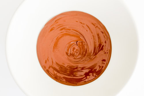 A swirl of smooth chocolate spread in a white bowl, reminiscent of Rocky Road candy, viewed from above.