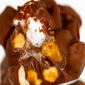 Close-up of a Rocky Road candy showcasing its rich chocolate coating, adorned with visible nuts and revealing a creamy white filling inside.