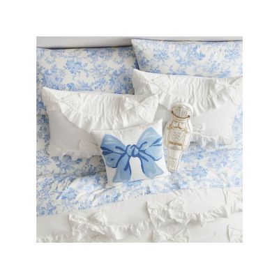 A bed with blue and white floral bedding, capturing the LoveShackFancy look for less, features decorative pillows: one with a charming blue bow design and another whimsically shaped like a teapot.