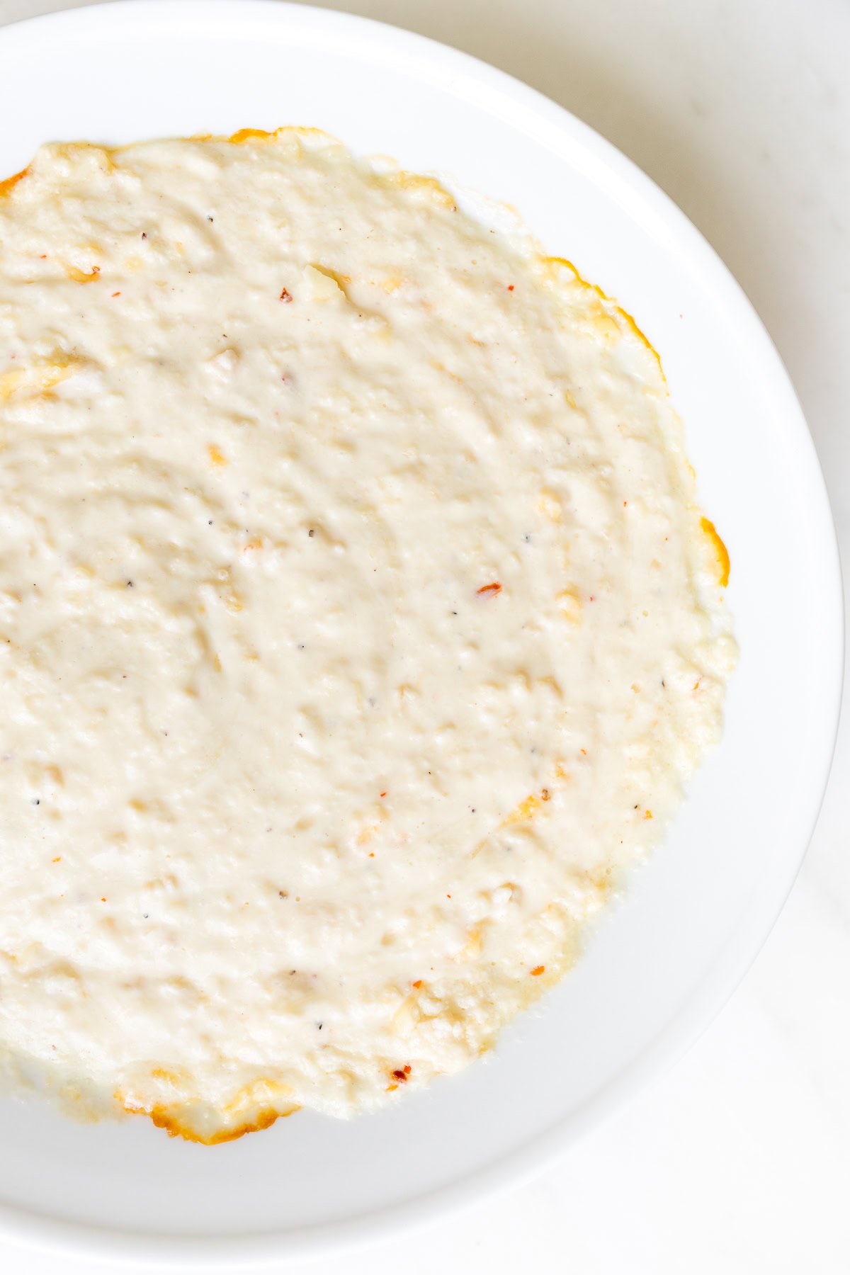 A thin layer of creamy Asiago Cheese Dip spread evenly on a white plate.