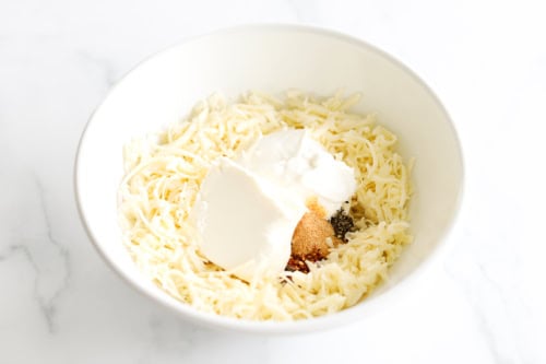 A bowl featuring a delightful Asiago Cheese Dip combines shredded cheese, cream cheese, and an array of spices.