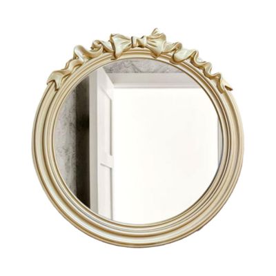 Round mirror with an ornate ribbon design on top reflects a partially visible white door, capturing the essence of LoveShackFancy's elegance for less.