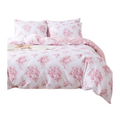 A bed with floral-patterned sheets and two pillows showcases a pink and white design reminiscent of LoveShackFancy. An open book and a cup sit elegantly on the side, creating a cozy look for less.