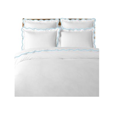 A neatly made bed showcases white bedding and four pillows, enhanced with subtle blue wavy trim, capturing that LoveShackFancy look for less.