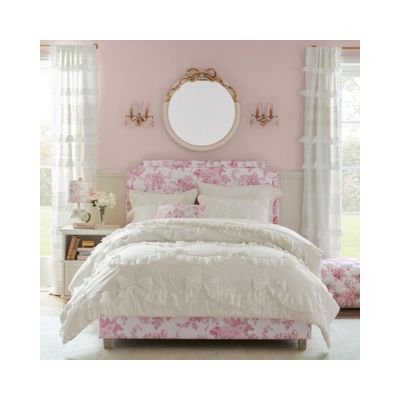 A pink and white bedroom exuding LoveShackFancy vibes, with floral patterns, a round mirror above the bed, and ruffled curtains for less.