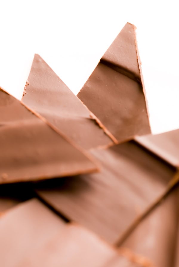 Close-up of several pieces of smooth, triangular milk chocolate overlapping each other against a white background.