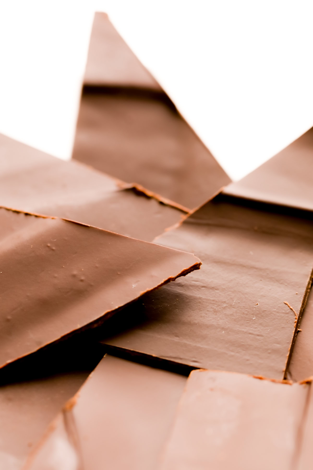 Close-up of several overlapping pieces of thin, broken chocolate shards on a white background.