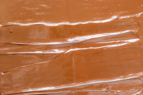 Close-up of smooth, glossy brown chocolate spread evenly, with visible streaks running across its surface.